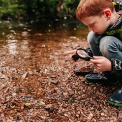 Junge mit Becherlupe am Bach