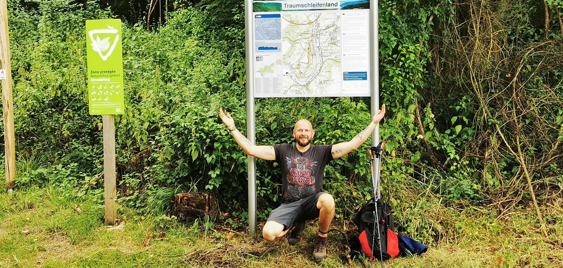 Ralf Künzer - Traumschleifenland Ralf Künzer kniet unter einer Tafel zur Traumschleife Traumschleifenland