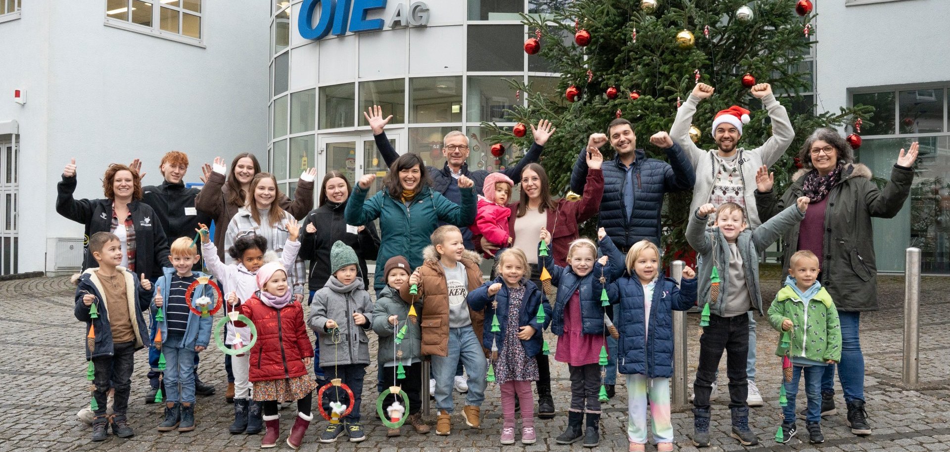Die Kinder der beiden Gewinner-Kindergärten präsentieren stolz ihren selbstgebastelten Fensterschmuck vor dem OIE Verwaltungsgebäude – gemeinsam mit Florian Schmidt, Kommunalbetreuer der OIE, und Thomas Johann, Vorstand der OIE.