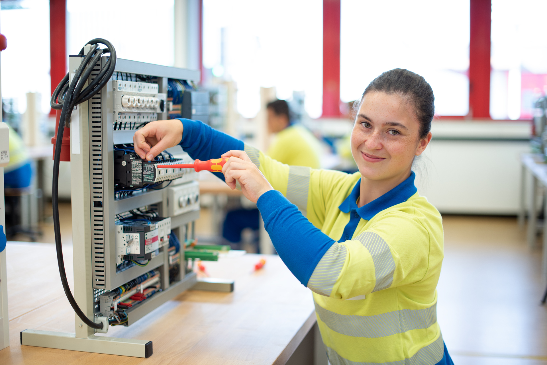 Westnetz Power-Praktikum. Eine junge Frau sitzt mit einem Schraubenzieher vor einer elektronischen Anlage.