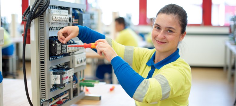 Westnetz Power-Praktikum. Eine junge Frau sitzt mit einem Schraubenzieher vor einer elektronischen Anlage.
