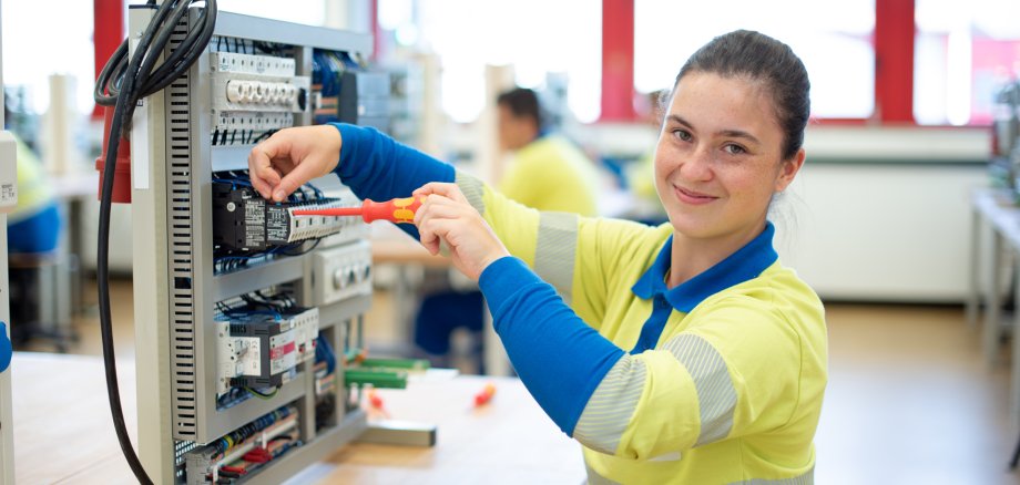 Westnetz Power-Praktikum. Eine junge Frau sitzt mit einem Schraubenzieher vor einer elektronischen Anlage.