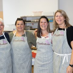 Die Damen vom Kuchenteam stehen zusammen am Bauernmarkt in Berglangenbach. Sie tragen alle ien Schürze mit dem Aufdruck "Kuchenteam"